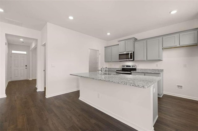 kitchen with gray cabinetry, a center island with sink, a sink, dark wood finished floors, and stainless steel appliances