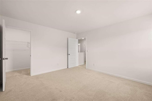 unfurnished bedroom with a spacious closet, baseboards, light colored carpet, recessed lighting, and a closet