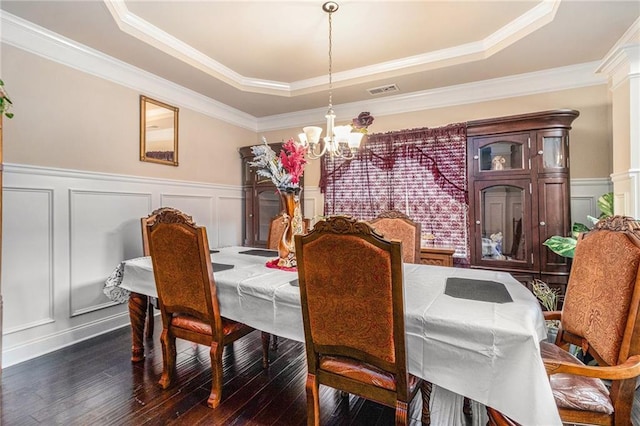 dining area with visible vents, dark wood finished floors, a tray ceiling, a notable chandelier, and a decorative wall