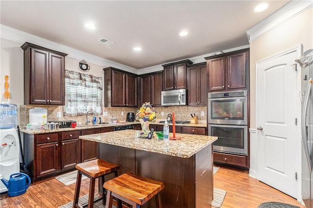 kitchen featuring dark brown cabinetry, visible vents, light wood finished floors, and stainless steel appliances