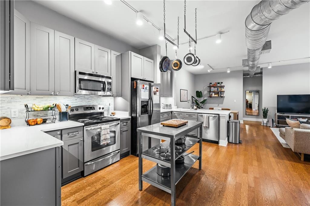 kitchen featuring sink, stainless steel appliances, light hardwood / wood-style floors, gray cabinets, and decorative backsplash