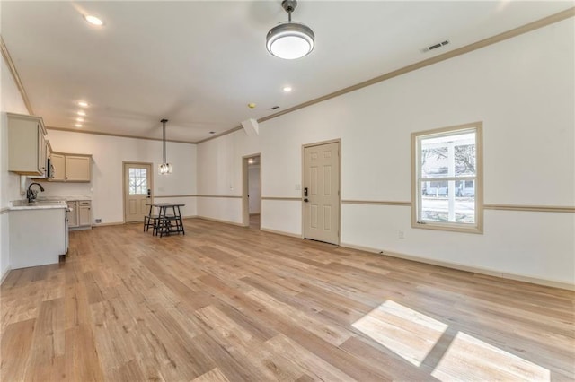 unfurnished living room with light wood finished floors, visible vents, crown molding, and a wealth of natural light