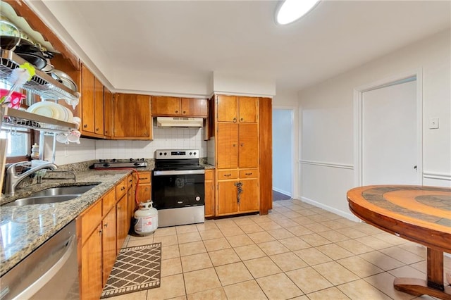 kitchen featuring light tile patterned floors, light stone counters, stainless steel appliances, sink, and decorative backsplash