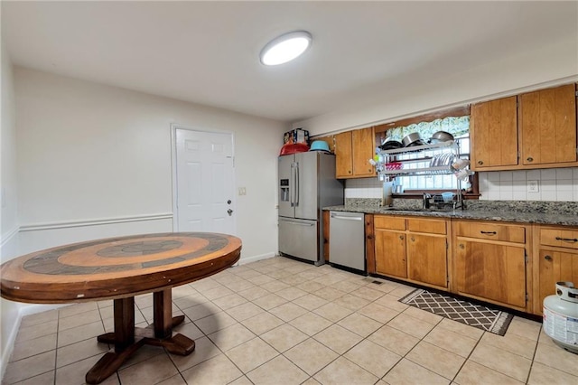 kitchen featuring light tile patterned flooring, appliances with stainless steel finishes, dark stone counters, and tasteful backsplash