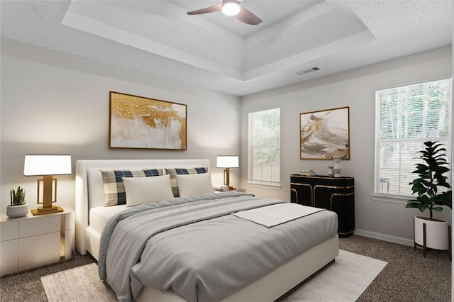 carpeted bedroom featuring a raised ceiling, ceiling fan, and a textured ceiling