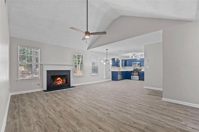 unfurnished living room featuring ceiling fan with notable chandelier, a healthy amount of sunlight, a textured ceiling, and light hardwood / wood-style flooring