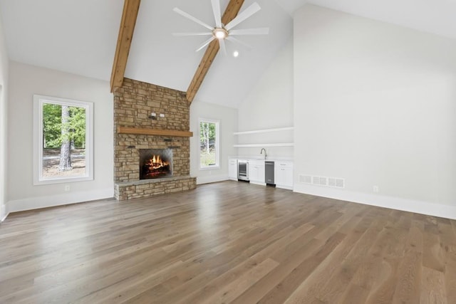 unfurnished living room featuring visible vents, beamed ceiling, wood finished floors, a stone fireplace, and high vaulted ceiling