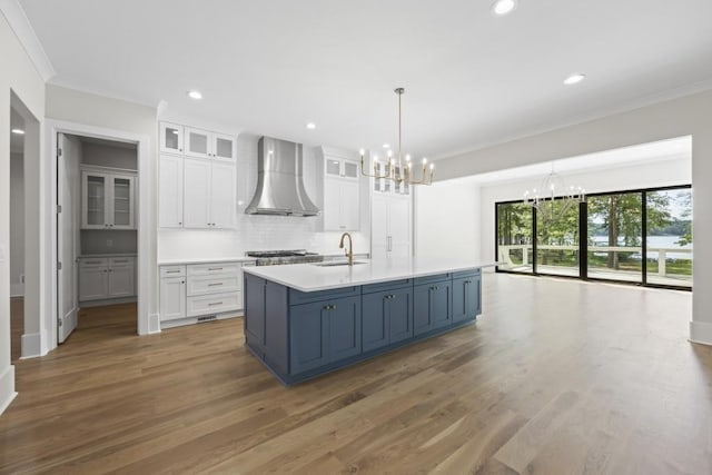 kitchen with glass insert cabinets, light countertops, white cabinetry, and wall chimney range hood