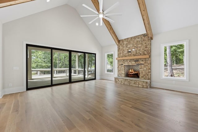 unfurnished living room featuring a healthy amount of sunlight, high vaulted ceiling, wood finished floors, and a stone fireplace