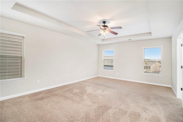 spare room with a raised ceiling, carpet flooring, baseboards, and ceiling fan