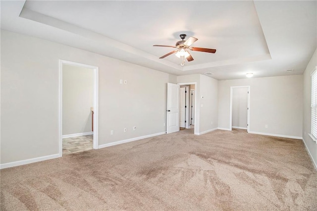 carpeted spare room featuring ceiling fan, baseboards, and a tray ceiling