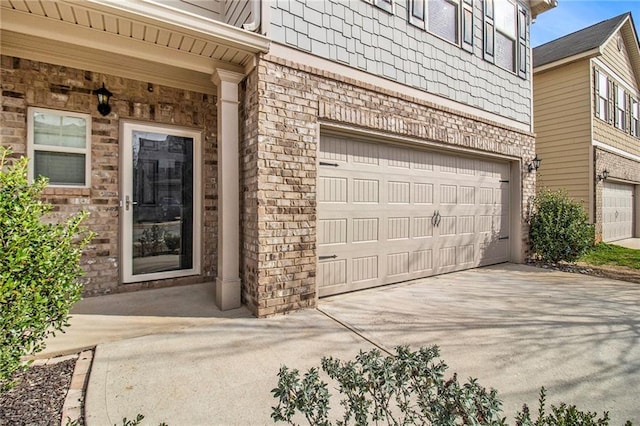 entrance to property featuring brick siding, an attached garage, and concrete driveway