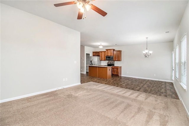 unfurnished living room featuring visible vents, ceiling fan with notable chandelier, baseboards, and dark carpet