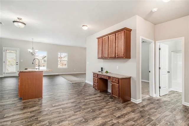 kitchen with brown cabinetry, baseboards, dark wood finished floors, a sink, and a notable chandelier