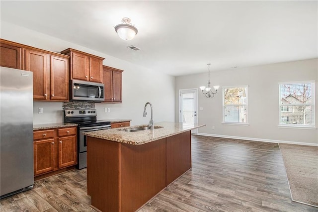 kitchen featuring light stone counters, dark wood finished floors, a sink, appliances with stainless steel finishes, and a notable chandelier