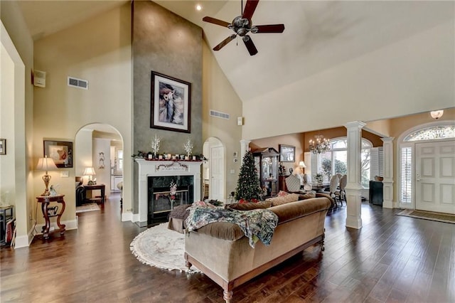 living room featuring ceiling fan with notable chandelier, a fireplace, high vaulted ceiling, and dark wood-type flooring