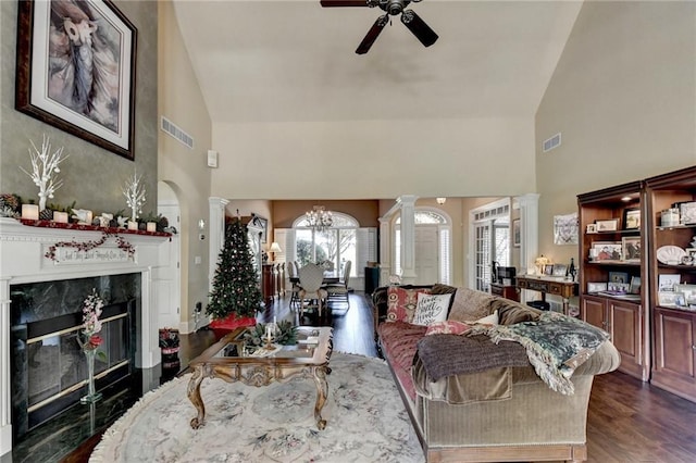 living room with ornate columns, high vaulted ceiling, dark hardwood / wood-style floors, a fireplace, and ceiling fan with notable chandelier