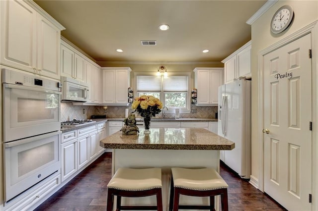 kitchen with a kitchen breakfast bar, dark hardwood / wood-style flooring, white appliances, a kitchen island, and white cabinetry