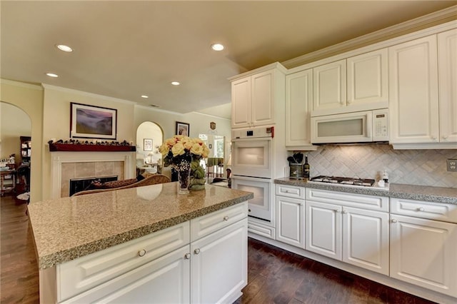 kitchen with white cabinetry, light stone countertops, white appliances, a tiled fireplace, and decorative backsplash