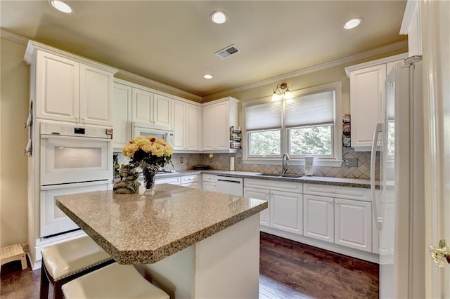 kitchen with white appliances, backsplash, sink, a kitchen bar, and white cabinetry