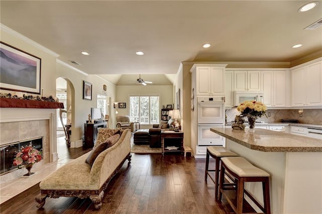 kitchen with a kitchen breakfast bar, tasteful backsplash, white appliances, white cabinetry, and a tiled fireplace