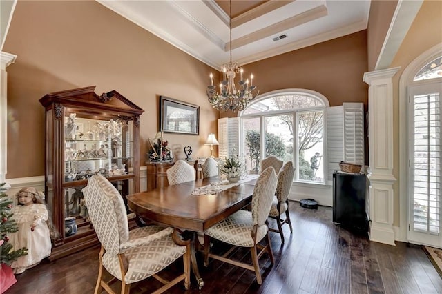 dining space featuring decorative columns, dark wood-type flooring, a raised ceiling, ornamental molding, and a chandelier