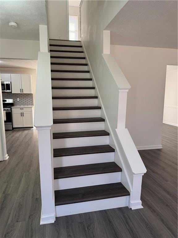 staircase featuring baseboards, a textured ceiling, and wood finished floors