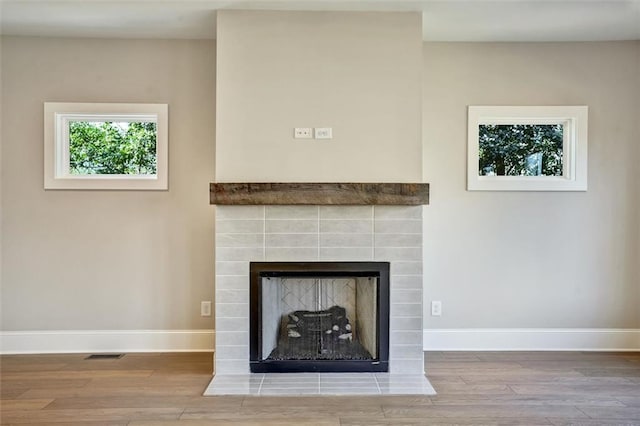 interior details featuring a tiled fireplace, wood finished floors, visible vents, and baseboards