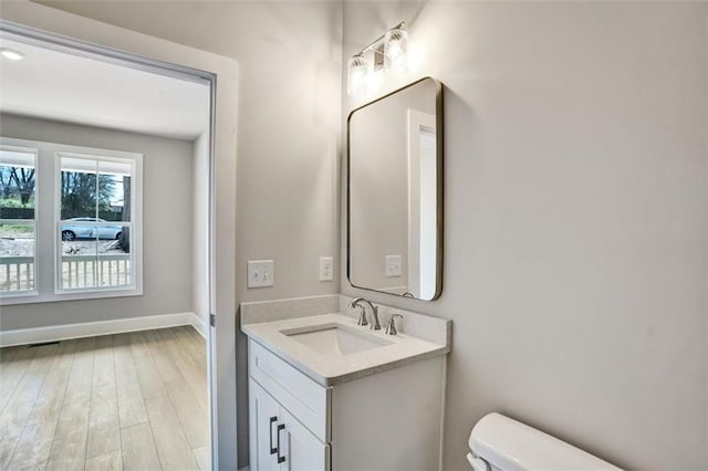 half bath featuring baseboards, vanity, toilet, and wood finished floors