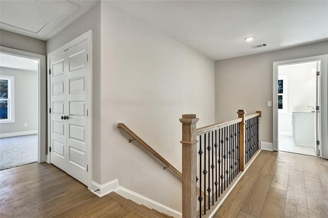 hallway with visible vents, baseboards, hardwood / wood-style floors, and an upstairs landing