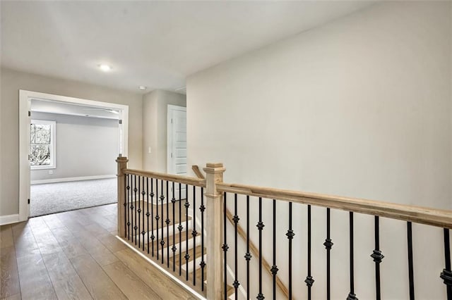 hall featuring wood finished floors, an upstairs landing, and baseboards