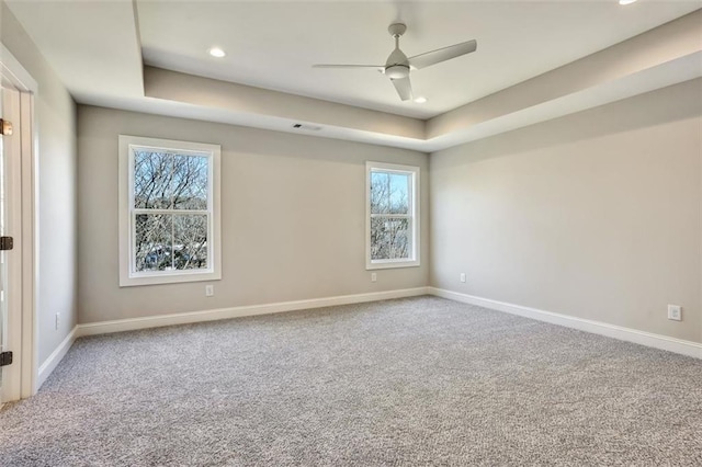 carpeted empty room with ceiling fan, a raised ceiling, and baseboards