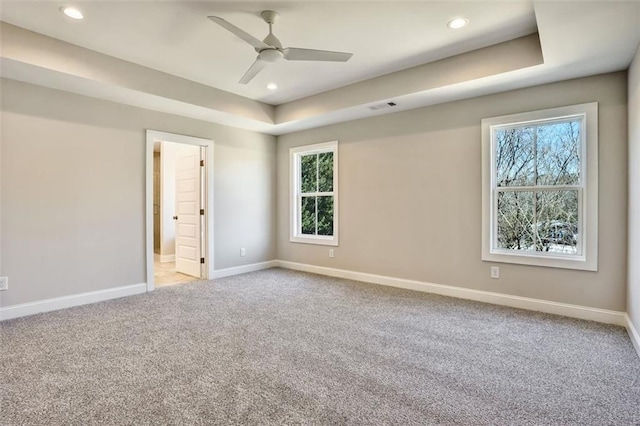 unfurnished room with a raised ceiling, light carpet, visible vents, and baseboards