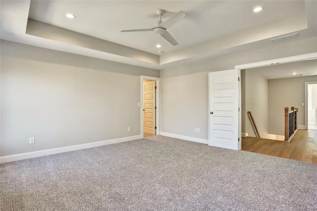 empty room with a tray ceiling, carpet flooring, baseboards, and recessed lighting