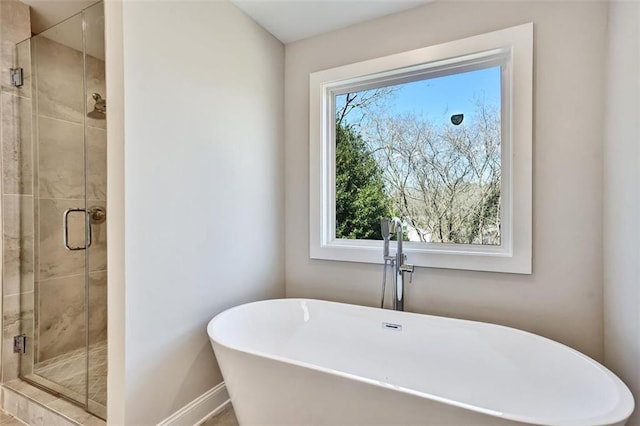 bathroom with a soaking tub, a shower stall, and baseboards