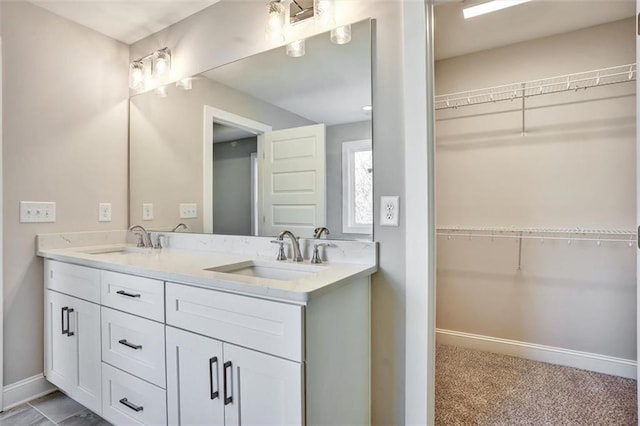 bathroom featuring a sink, a spacious closet, baseboards, and double vanity