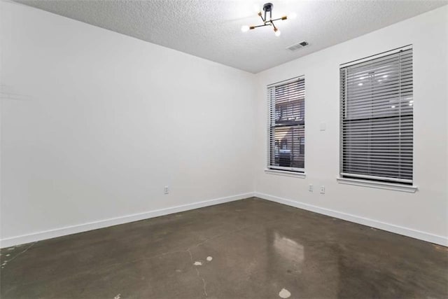 spare room with concrete floors, a textured ceiling, visible vents, and baseboards