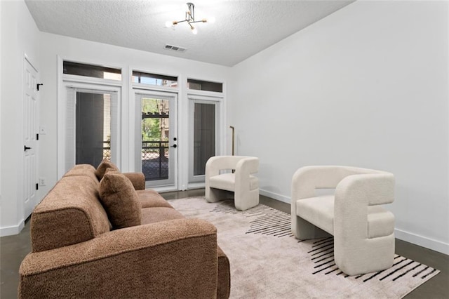 living area with a textured ceiling, visible vents, baseboards, and a notable chandelier