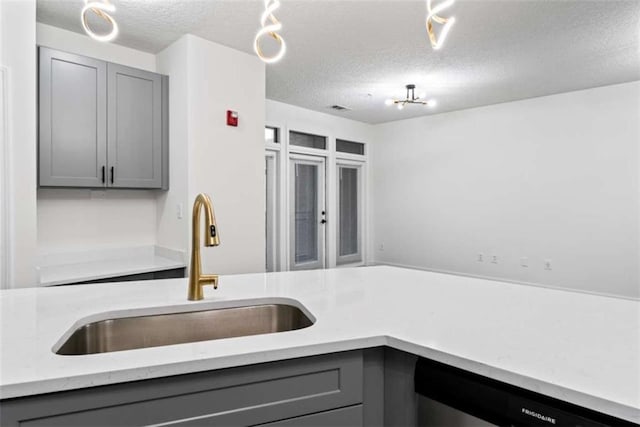 kitchen with a textured ceiling, stainless steel dishwasher, a sink, and gray cabinetry