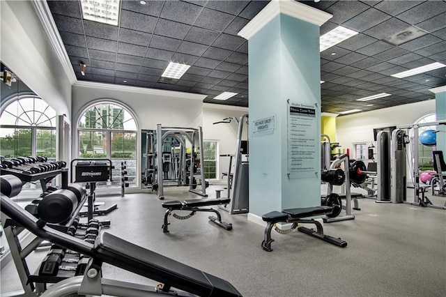 exercise room with a paneled ceiling, crown molding, and baseboards