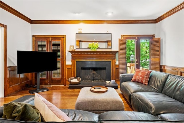 living room featuring wood finished floors, ornamental molding, wainscoting, and a fireplace with raised hearth