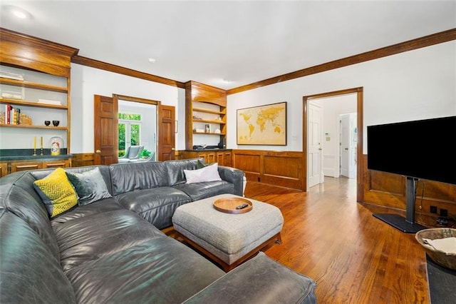 living room featuring ornamental molding, wood finished floors, built in shelves, and a wainscoted wall