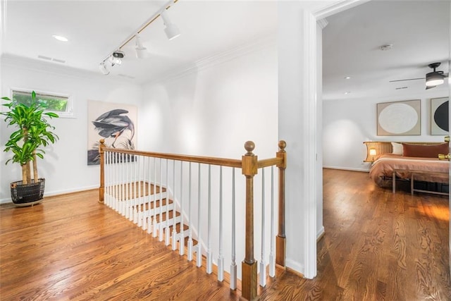 hall featuring an upstairs landing, rail lighting, crown molding, wood finished floors, and baseboards