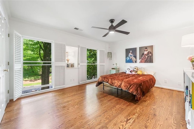 bedroom featuring multiple windows, wood finished floors, ornamental molding, baseboards, and a ceiling fan