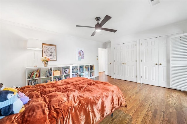 bedroom with wood finished floors, multiple closets, a ceiling fan, and crown molding