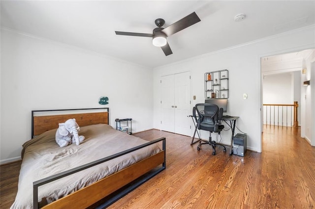 bedroom with ornamental molding, wood finished floors, a closet, baseboards, and a ceiling fan