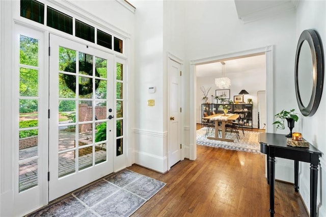 foyer entrance with wood finished floors, crown molding, and a chandelier