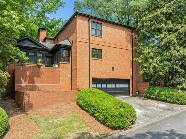 view of home's exterior with a garage, brick siding, a chimney, and driveway