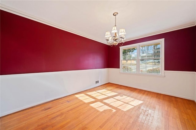 empty room featuring an inviting chandelier, ornamental molding, and hardwood / wood-style flooring