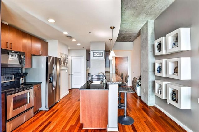 kitchen featuring kitchen peninsula, hanging light fixtures, a breakfast bar, appliances with stainless steel finishes, and sink